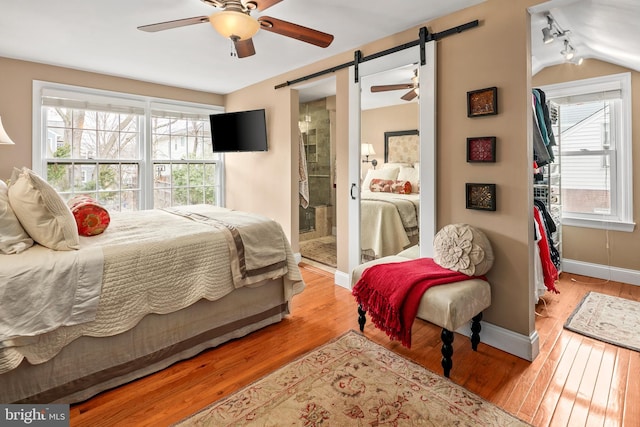 bedroom with lofted ceiling, wood finished floors, a barn door, baseboards, and ceiling fan