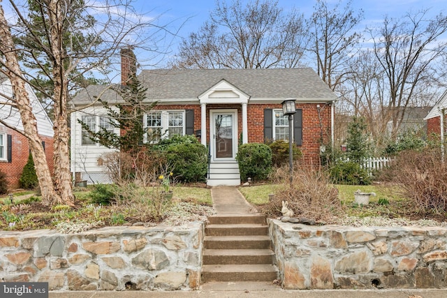 view of front of house featuring brick siding, roof with shingles, a chimney, and entry steps