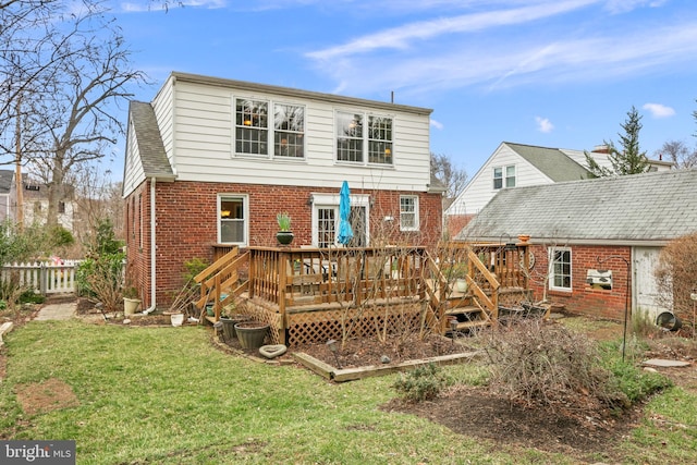 rear view of property featuring fence, roof with shingles, a wooden deck, a lawn, and brick siding