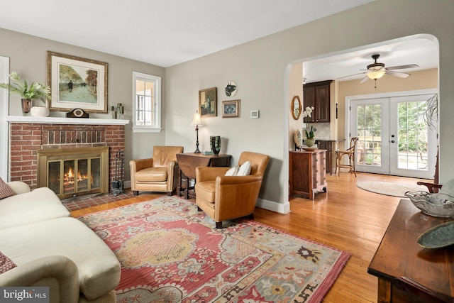 living area featuring plenty of natural light, a brick fireplace, french doors, and light wood-style floors