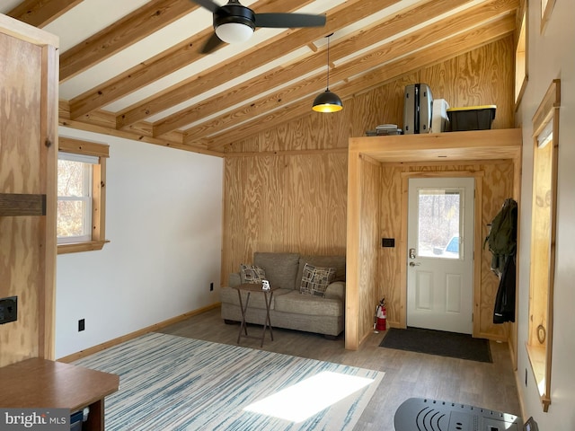 interior space featuring lofted ceiling with beams, wood finished floors, baseboards, and wood walls