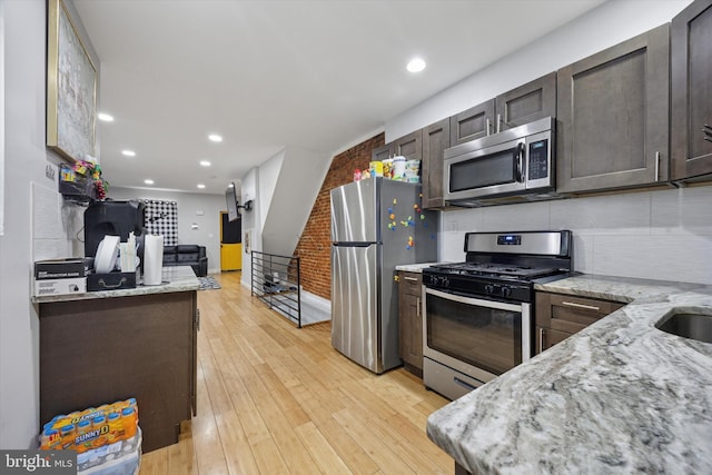 kitchen featuring dark brown cabinetry, stainless steel appliances, light wood-style floors, and light stone countertops