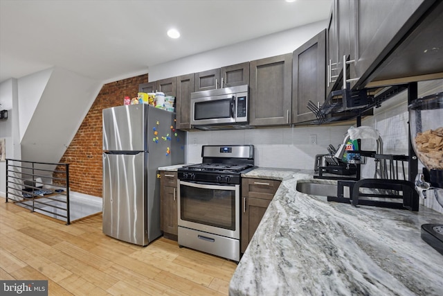 kitchen with light stone counters, brick wall, appliances with stainless steel finishes, light wood-type flooring, and backsplash