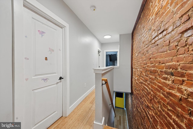 corridor featuring an upstairs landing, baseboards, brick wall, and light wood finished floors