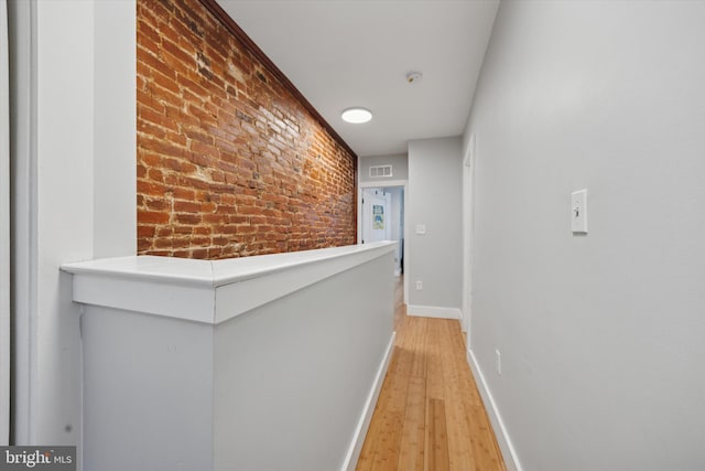 hallway with light wood-type flooring, visible vents, baseboards, and brick wall