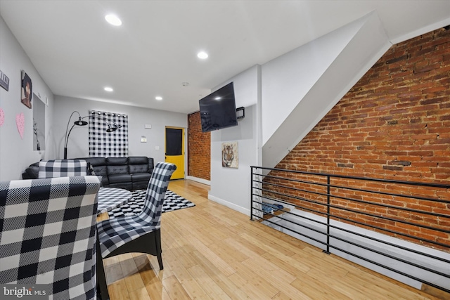 living room featuring hardwood / wood-style flooring, recessed lighting, baseboards, and brick wall