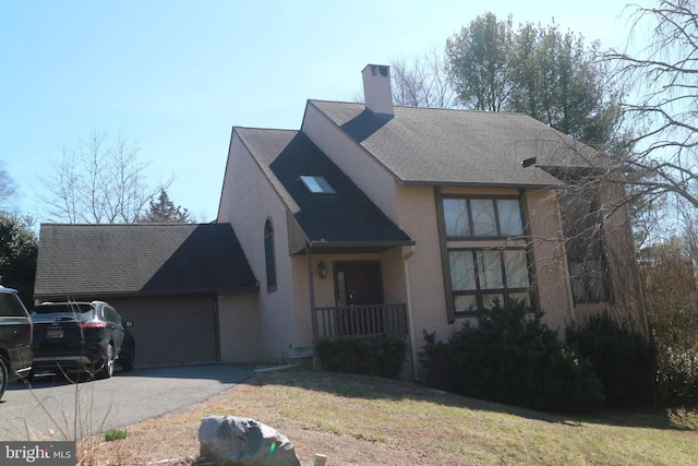 view of front of house featuring roof with shingles, a chimney, driveway, and stucco siding