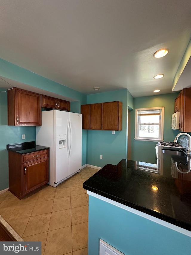 kitchen with light tile patterned flooring, brown cabinets, white appliances, and dark countertops