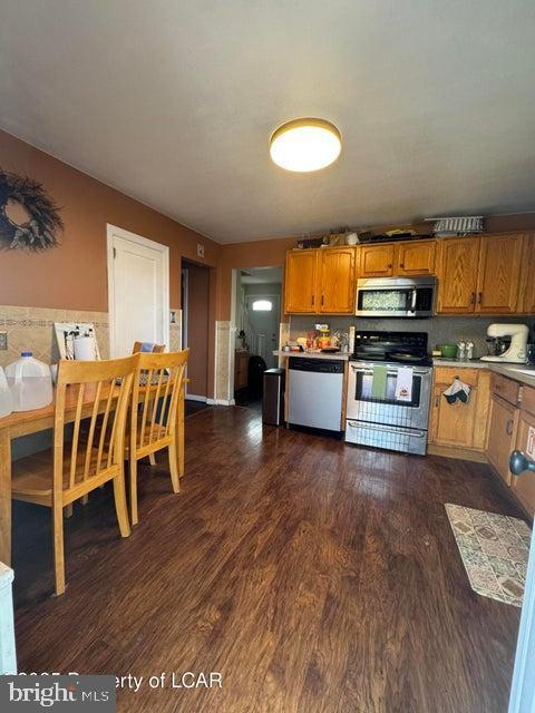 kitchen with light countertops, brown cabinetry, dark wood-style flooring, and appliances with stainless steel finishes