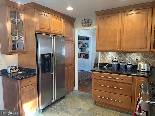 kitchen with brown cabinets, dark stone countertops, range with gas cooktop, stainless steel fridge, and glass insert cabinets