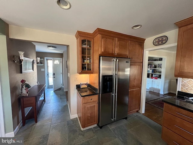 kitchen featuring glass insert cabinets, stone tile floors, stainless steel fridge with ice dispenser, and baseboards