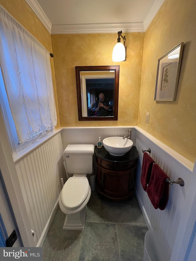 half bath with a wainscoted wall, vanity, toilet, and crown molding