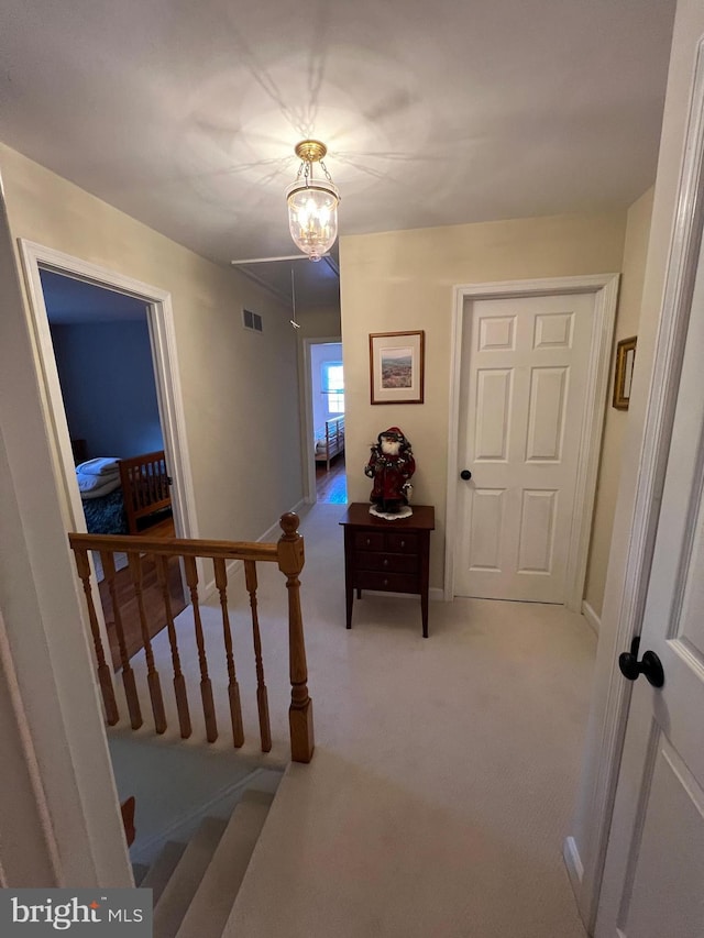 hallway featuring attic access, light colored carpet, visible vents, and baseboards