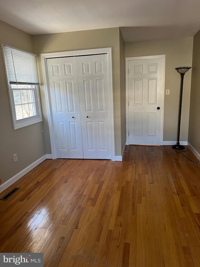 unfurnished bedroom with hardwood / wood-style floors, baseboards, visible vents, and a closet