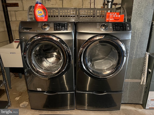 washroom featuring laundry area, concrete block wall, separate washer and dryer, and a sink