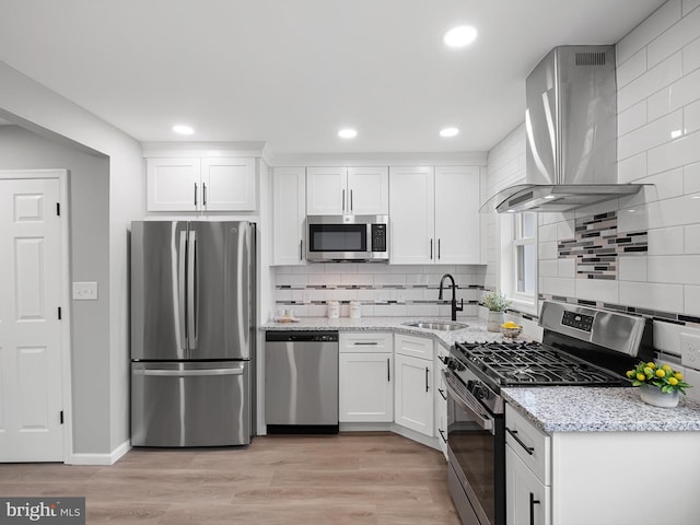 kitchen with extractor fan, light wood-style floors, white cabinets, stainless steel appliances, and a sink