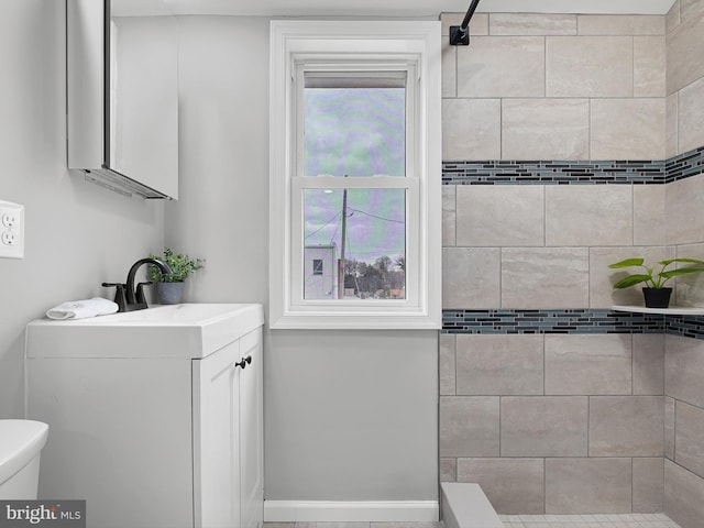 bathroom with vanity, toilet, baseboards, and tiled shower