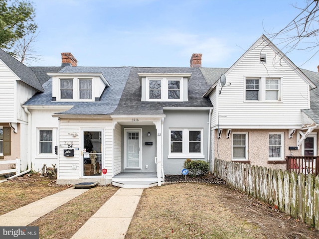 view of front of house with a shingled roof, a chimney, and fence