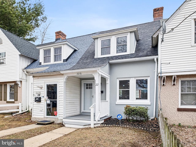 view of front of house with stucco siding, a chimney, and a shingled roof