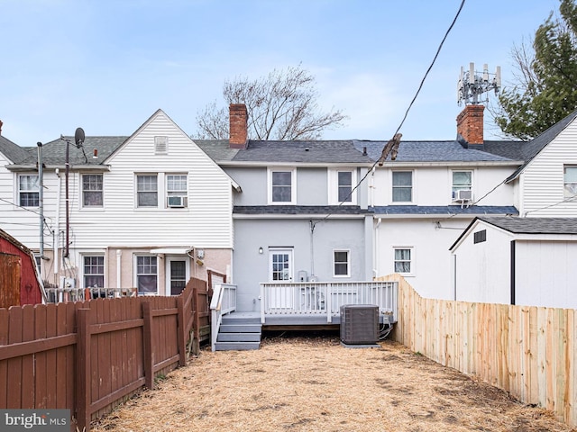 back of property with a wooden deck, central AC unit, a fenced backyard, and a chimney