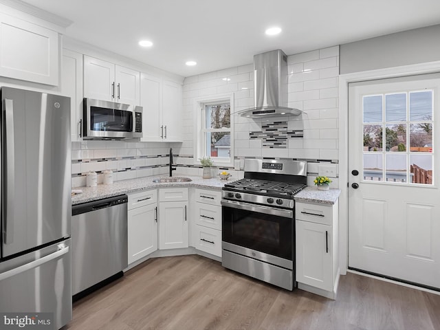 kitchen with a sink, stainless steel appliances, light wood finished floors, and wall chimney range hood