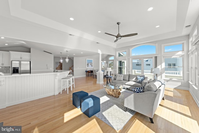 living room with a tray ceiling, recessed lighting, light wood-type flooring, and ornate columns