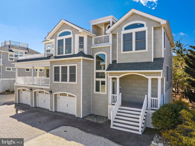 view of front facade with an attached garage, a shingled roof, covered porch, a balcony, and driveway