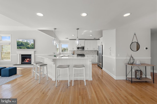 kitchen with stainless steel appliances, white cabinets, light wood-style floors, a kitchen bar, and open floor plan