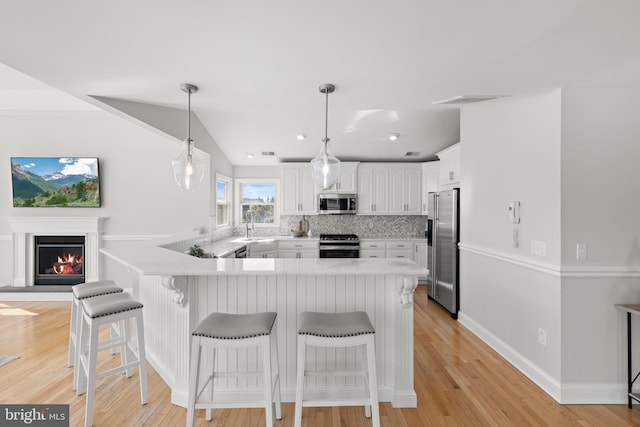 kitchen with a kitchen breakfast bar, white cabinets, a peninsula, and appliances with stainless steel finishes