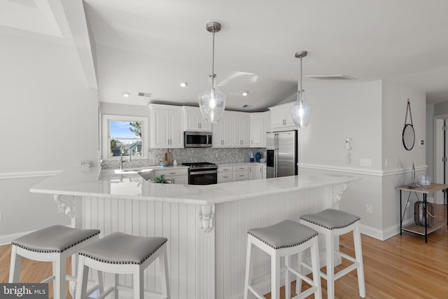 kitchen with a peninsula, stainless steel appliances, light wood-style floors, white cabinetry, and tasteful backsplash