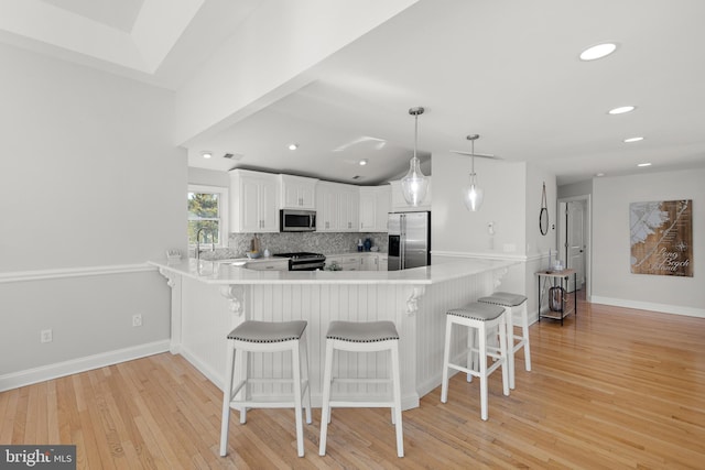 kitchen with a sink, backsplash, white cabinetry, appliances with stainless steel finishes, and a peninsula