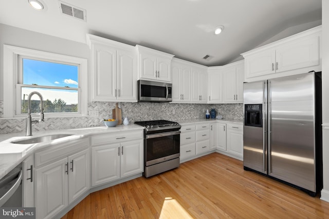 kitchen featuring visible vents, a sink, stainless steel appliances, vaulted ceiling, and white cabinets