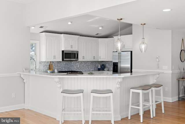 kitchen featuring a peninsula, white cabinets, backsplash, and stainless steel appliances