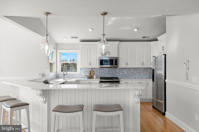 kitchen featuring visible vents, a peninsula, a sink, stainless steel appliances, and white cabinetry