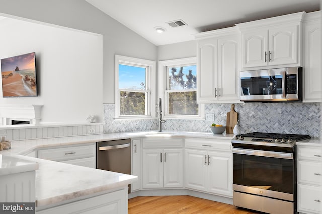 kitchen with visible vents, a sink, white cabinetry, stainless steel appliances, and vaulted ceiling