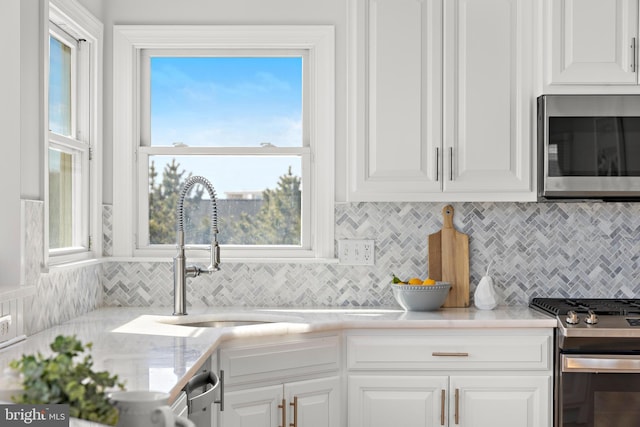 kitchen featuring a sink, backsplash, appliances with stainless steel finishes, and white cabinetry