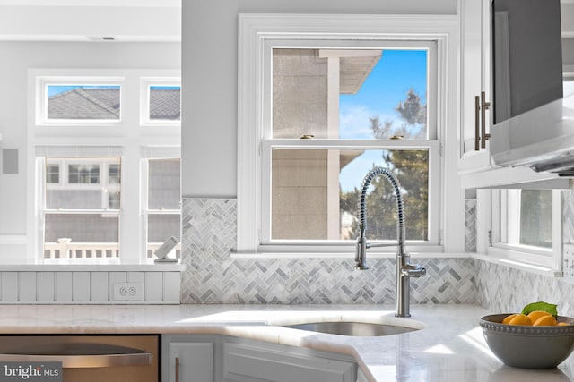 kitchen with tasteful backsplash, white cabinets, stainless steel dishwasher, and a sink