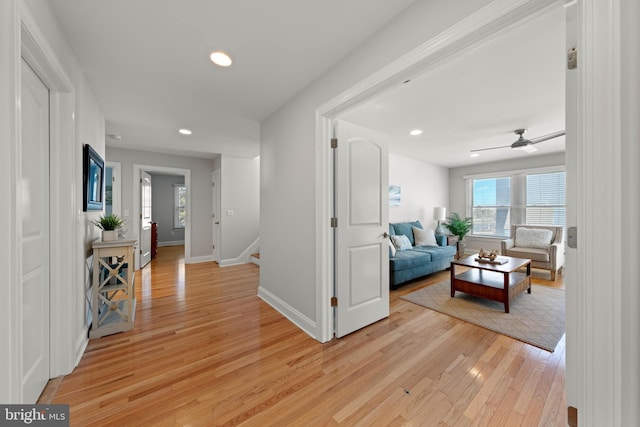 corridor featuring recessed lighting, light wood-type flooring, baseboards, and stairs