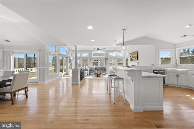 kitchen featuring open floor plan, vaulted ceiling, light wood-style flooring, ornate columns, and a sink