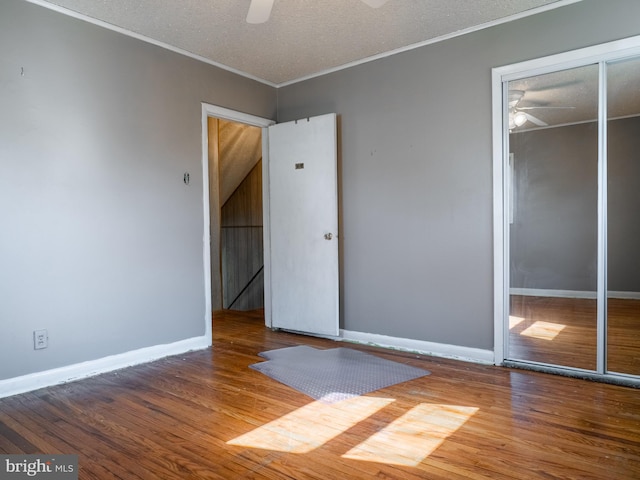 unfurnished bedroom with baseboards, ornamental molding, wood finished floors, a closet, and a textured ceiling