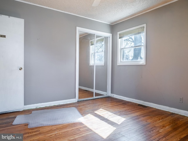 unfurnished bedroom with wood finished floors, visible vents, a closet, a textured ceiling, and crown molding