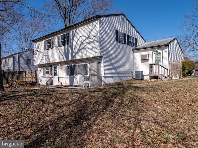 back of property with an AC wall unit, a yard, central AC, and fence