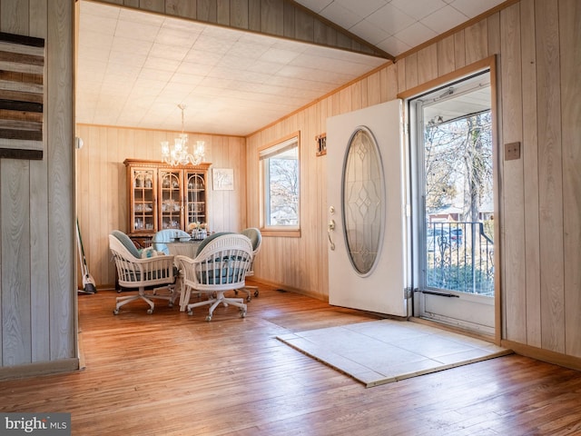 foyer entrance with lofted ceiling, a notable chandelier, wood finished floors, and wood walls