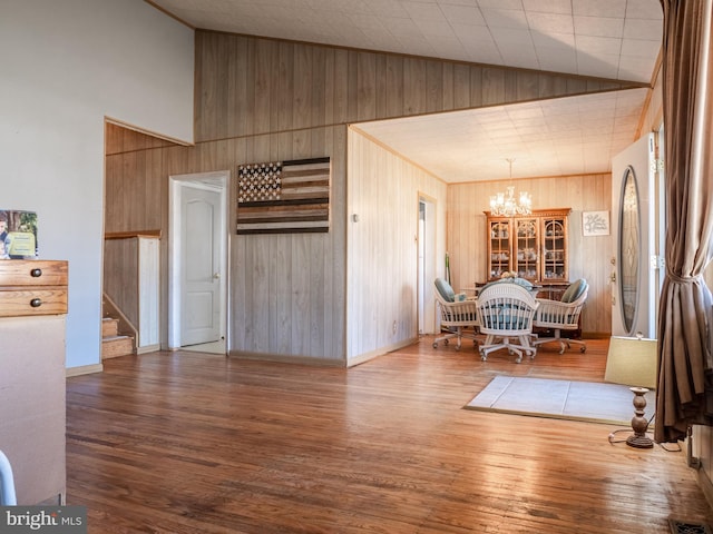 unfurnished dining area featuring high vaulted ceiling, wood finished floors, stairway, wooden walls, and a chandelier