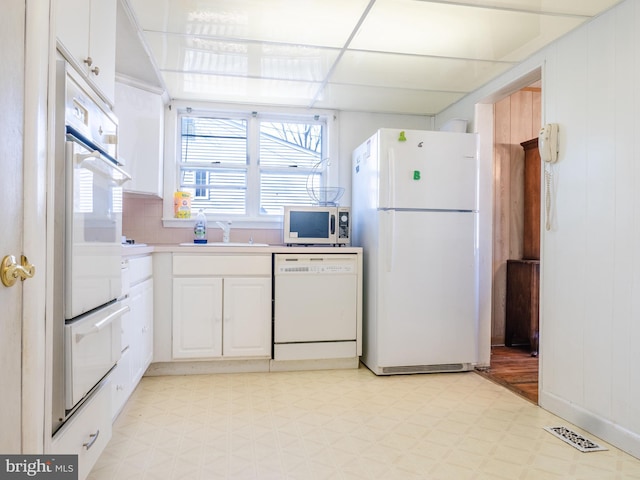 kitchen with visible vents, light floors, white cabinets, white appliances, and a sink