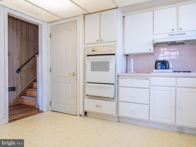 kitchen featuring under cabinet range hood, light floors, light countertops, white oven, and a warming drawer