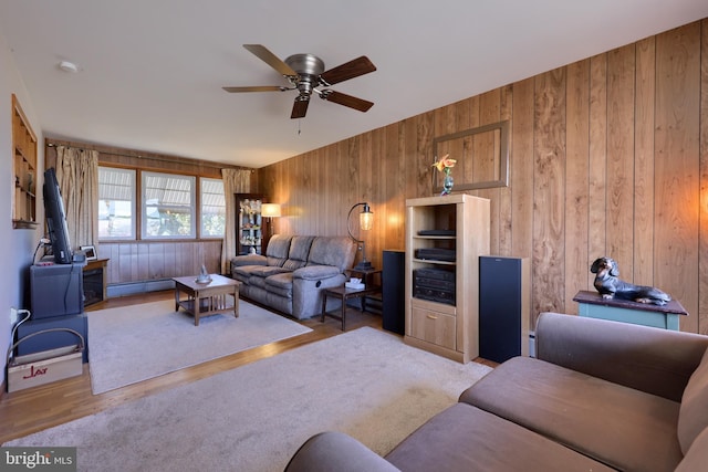 living room with wooden walls, a baseboard heating unit, ceiling fan, a wood stove, and wood finished floors