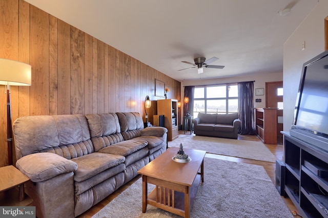 living room featuring wood walls, a ceiling fan, and light wood finished floors