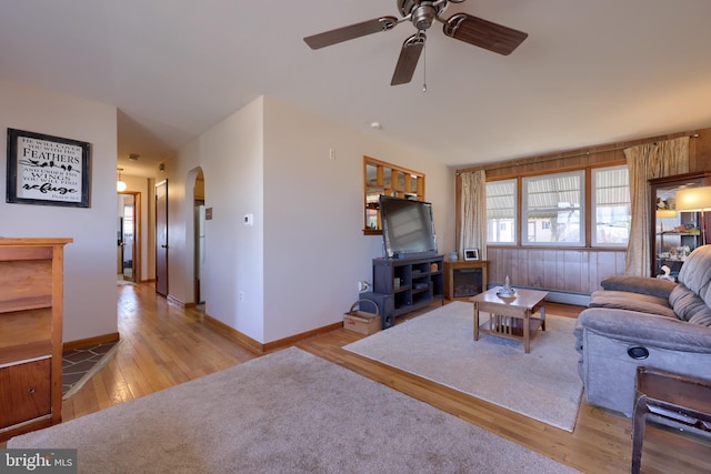 living area with baseboards, arched walkways, a ceiling fan, and hardwood / wood-style flooring