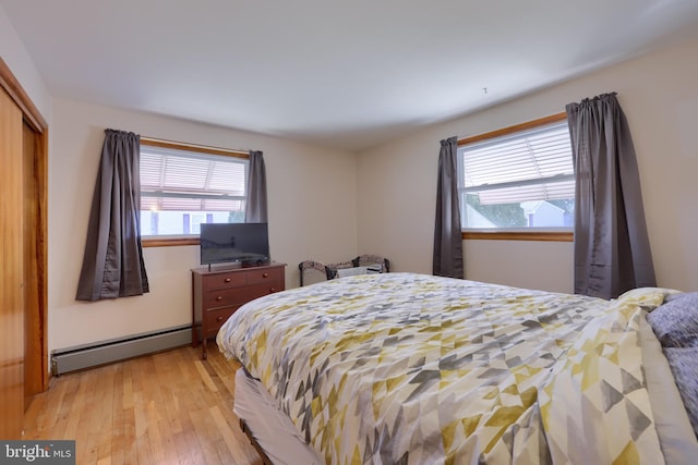 bedroom with a baseboard radiator, multiple windows, light wood-style floors, and a closet